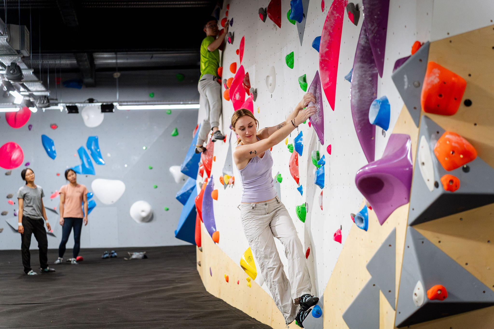 Woman climbing at a bouldering gym while friends look on