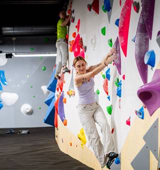 Woman climbing at a bouldering gym while friends look on