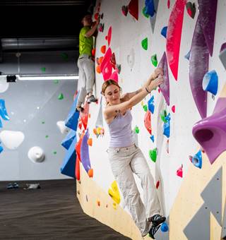 Woman climbing at a bouldering gym while friends look on